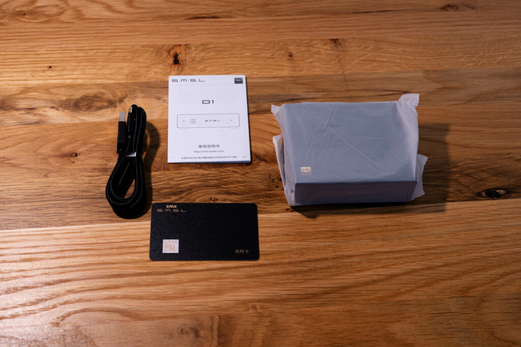 SMSL D1 - Blick auf die Garantiekarte, Kurzanleitung, USB-Kabel und das Gerät selber in milchigem Beutel